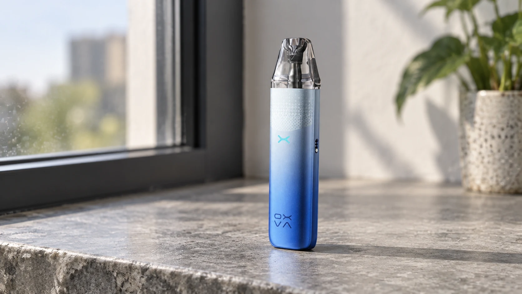 Blue OXVA NeXLIM 2 Mini pod vape standing on a sunlit stone windowsill beside a blurred plant.