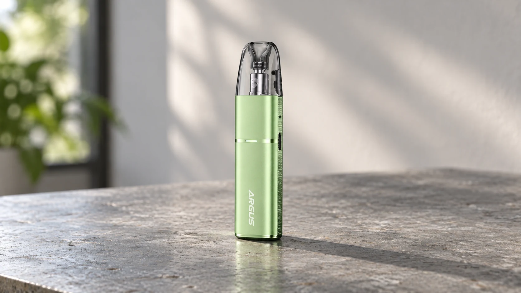 Green VOOPOO ARGUS G3 Mini pod vape standing upright on a stone countertop in soft window light.